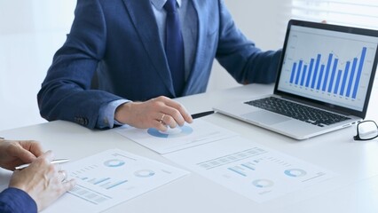 Business colleagues discussing financial data on a laptop and printed documents while analyzing charts and market trends. Business people and finance concept