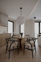 Modern minimalist dining room with wooden furniture and a unique pendant light. Natural light illuminates the space with clean lines and neutral tones.