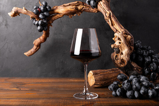 A glass of red wine with a composition of old wood and grape. Minimalistic composition with black background