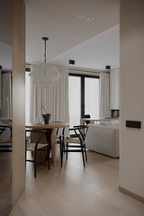 A cozy, modern living space with a dining area featuring wooden furniture and a large window. Soft lighting enhances the serene atmosphere.