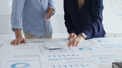 Business colleagues are examining financial data, pointing at charts and graphs spread out on a table during a collaborative analysis session in a modern office.