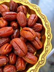 Close up of dried dates in a decorative golden bowl with ornate carvings and a blurred background