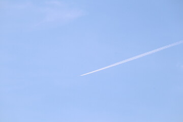 Skyward Trail: A contrail streaks across a vast, tranquil, light blue sky, symbolizing the journey of flight and travel, inviting the viewer to imagine endless possibilities.