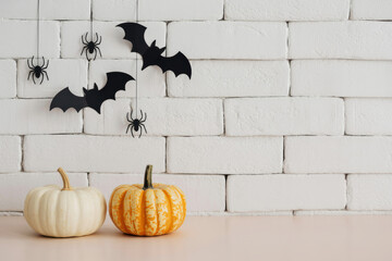 Modern spooky vignette with pumpkins, spiders, and bats on white wall background