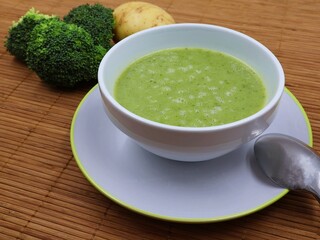 Broccoli soup in a soup bowl with potatoes and broccoli in the background.