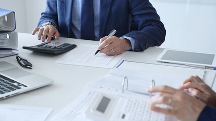 Fototapeta premium Close up of female accountant hands using calculator while collaborating with male colleague in office, calculating taxes and analyzing financial data. Audit and taxes in business
