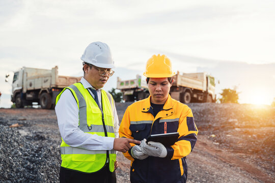 Construction site teamwork, safety gear, tablet usage, project discussion, collaboration, professional workers, sunset background, mining industry