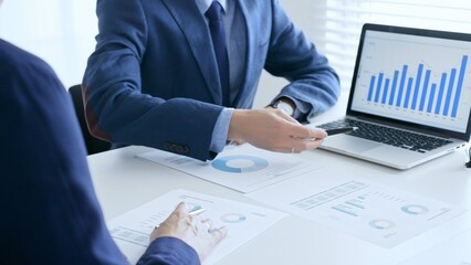 Business colleagues discussing financial data on a laptop and printed documents while analyzing charts and market trends. Business people and finance concept