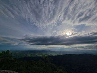 Skyward Panorama: A vast panorama of rolling hills and valleys unfolds beneath a dramatic sky, the sun peeking through a tapestry of clouds. Awe-inspiring spectacle of nature