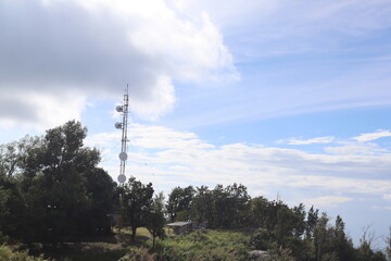 Obraz premium Tower in the Sky: A towering telecommunications structure stands against the backdrop of a bright sky, surrounded by a lush environment.