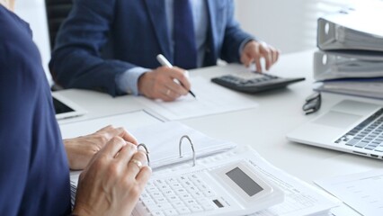 Close up of female accountant hands using calculator while collaborating with male colleague in office, calculating taxes and analyzing financial data. Audit and taxes in business