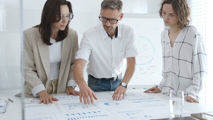 Professional team analyzing financial charts, colleagues reviewing data with focused expressions in modern workplace setting. Business people concept