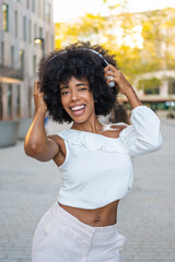 Young woman listening music with headphones and dancing in the street