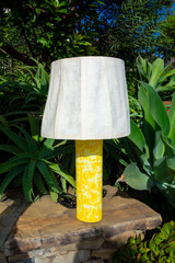 Yellow table lamp with paper lampshade set in front of some nice landscaping.
