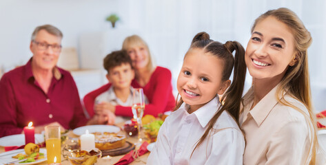 Portrait of happy multi generation family sitting at festive table, looking at camera and smiling. Kids, parents and grandparents celebrating holiday together, having festive meal at home