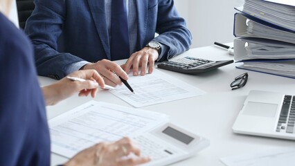 Accountants analyzing financial documents, calculating numbers together at shared workspace with laptop and office supplies surrounding them. Audit and taxes in business