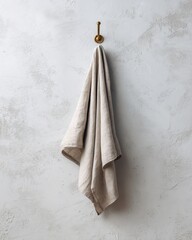 Fototapeta premium Natural linen towel hanging on a vintage brass hook against a textured gray wall.