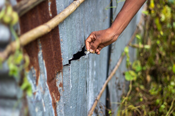 A hand reaching into a crack in a rusty corrugated metal wall