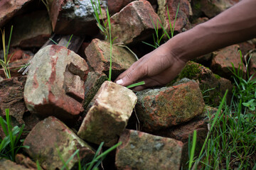 Hand reaching for old bricks with green grass growing around them