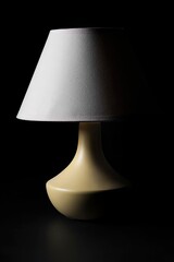 Minimalist lamp with beige base and white shade on dark background
