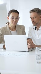 Obraz premium Businessman and adult businesswoman reviewing marketing analytics on laptops, working together strategically in contemporary office workplace. Business people concept