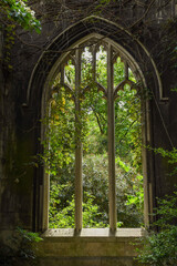 Obraz premium Abandoned St Dunstan in the East Church, featuring a gothic window surrounded by overgrown plants, showcasing a blend of architecture and nature.