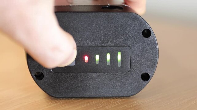 Finger pressing test button on high capacity lithium ion battery. Status LEDs activate showing full charge level and operational readiness. Close up technical view of rechargeable energy storage unit.