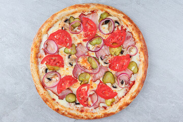 Pizza with Bacon, Tomatoes, Pickles, Red Onion, Mushrooms, and Melted Cheese on Baked Crust over Gray Stone Background