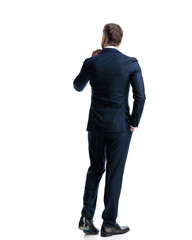 back view of elegant businessman in navy blue suit walking with hand in pocket