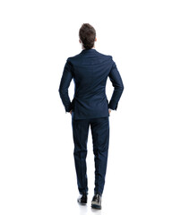back view of elegant man in navy blue suit walking with hands in pockets