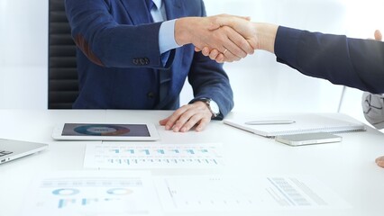 Business partners shaking hands at a meeting, celebrating successful negotiations and signing a contract, with documents, digital tablet, and smartphone on the table