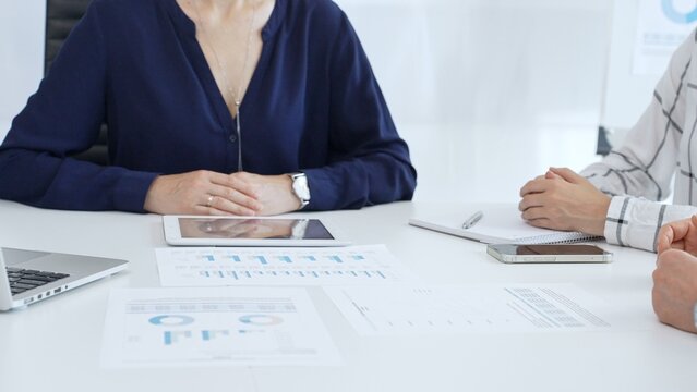 Professional women collaborating in workplace, reviewing financial analytics on digital devices and printed reports, sharing strategic insights