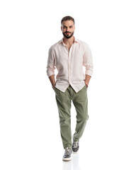 Fototapeta premium handsome young man with beard smiling and walking with hands in pockets
