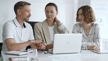 Professional team reviewing project data on laptop, working together in modern office environment, collaborating with focused corporate energy