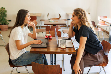 two girlfriends working on laptops and enjoying a conversation in a cozy cafe setting