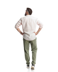 rear view of casual bearded man walking with hands on hips and looking up