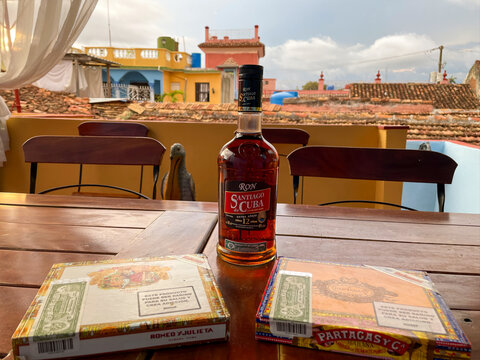Trinidad, Cuba. Ron Santiago de Cuba rum, Romeo y Julieta and Partagas cigar boxes on a terrace table, colorful colonial rooftops