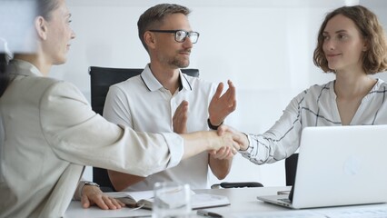 Obraz premium Businesswomen partners are shaking hands after successful negotiation, colleagues clapping, celebrating agreement in modern office headset. Handshake concept