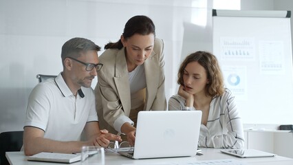 Business team collaborating on a project, analyzing data on a laptop during a productive office meeting, demonstrating teamwork and problem solving skills