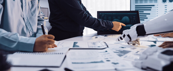 A diverse business team is engaged in data analysis, combining human insights with robotics technology in a modern office setting to drive informed decisions.Noogenesis