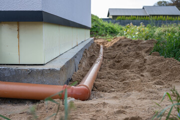 Residential construction with newly installed underground drainage pipe next to insulated house foundation and sand backfill.