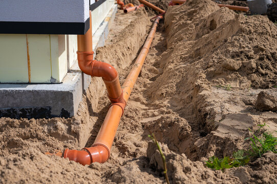 Underground drainage pipe installation next to residential building foundation during construction.