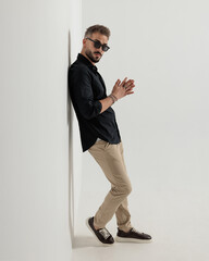 confident cool man with sunglasses rubbing palms and leaning on a wall