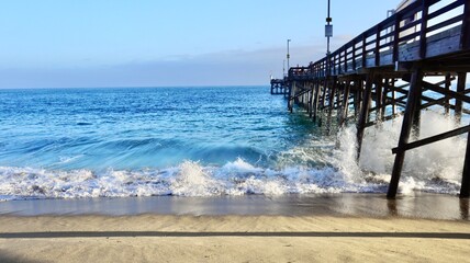 Wooden pier and waves breaking on sandy beach at California coast