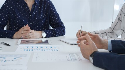 Professional colleagues examining financial documents, studying performance charts on paper and digital tablet during collaborative meeting in modern workplace setting