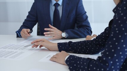 Business professionals analyzing contract details, gesturing with pens while discussing legal terms during collaborative meeting, focused on negotiation process