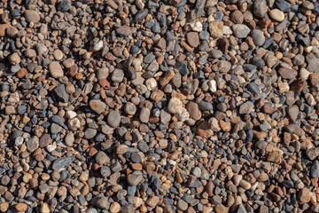 A top-down view of numerous small and medium-sized river rocks. The stones, mostly gray and brown, are scattered across the ground,