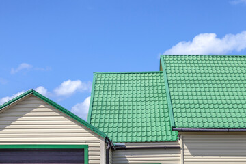 House with a green roof and white siding sits under a clear blue sky. The roof is made of metal and has a green trim, giving the house a unique and eye-catching appearance
