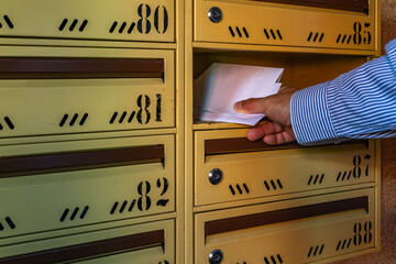 A man takes a letter out of a mailbox, a man puts a letter into a mailbox in an apartment building,
