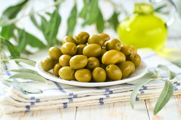 Green olives in bowl with fresh olive leaves. Greens olives on a white wooden table.